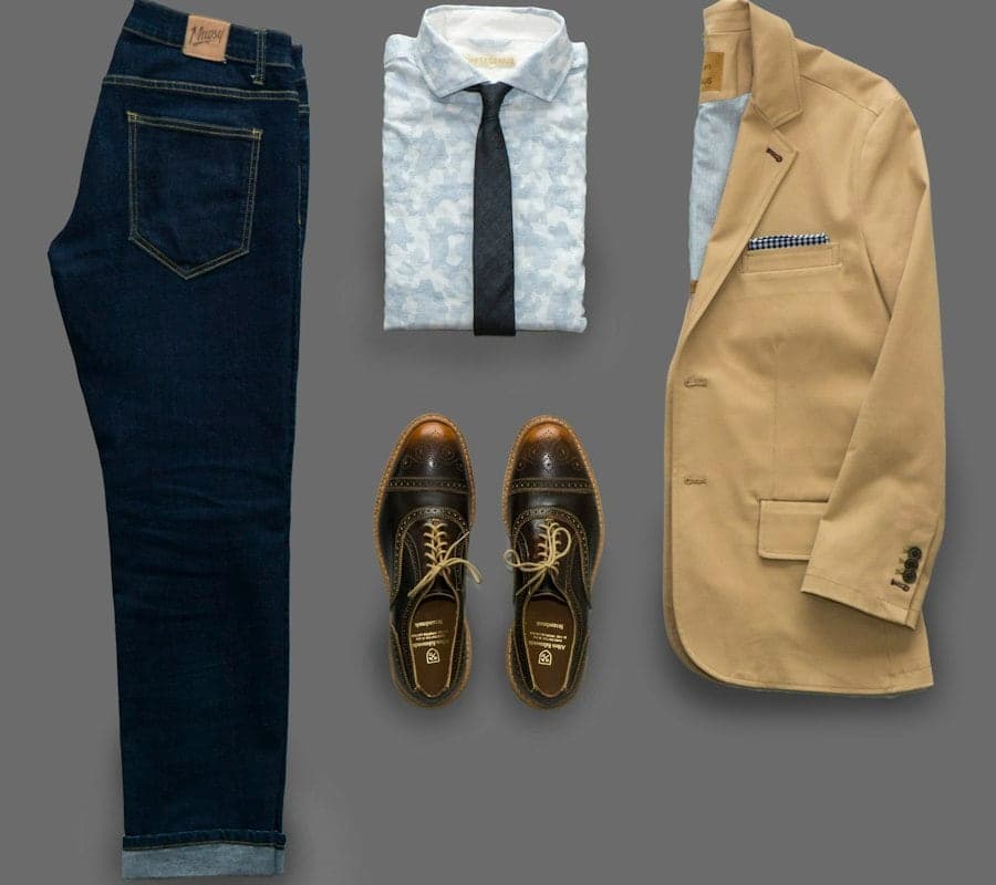Navy trousers, brown brogues and a tan blazer arranged flat on a grey background