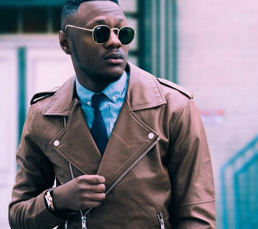 A man wearing a tan leather jacket over a light blue shirt and navy tie